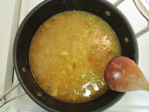 Potato leek soup simmering in a black pot with chopped ingredients and a wooden spoon.