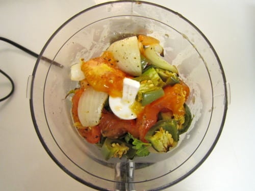 Roasted tomatoes, onions, jalapeños, garlic, and cilantro in a food processor, prepared for making roasted tomato salsa for carne asada tacos.