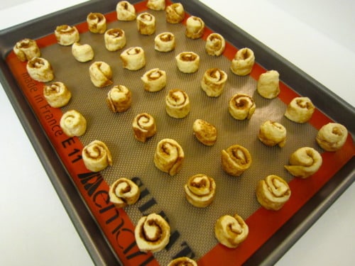Mini cinnamon roll bites arranged on a silicone baking mat-lined baking sheet, ready for baking.