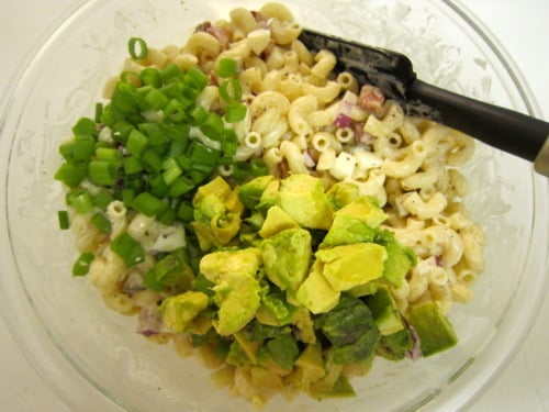 Macaroni salad in a glass bowl with diced avocado and chopped green onions before mixing