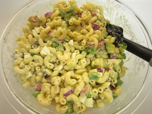 Macaroni salad in a glass bowl mixed with pancetta, avocado, red onion, green bell pepper, and a creamy dressing.