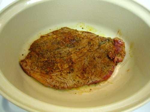 Seasoned beef chuck roast searing in a large oval pot, prepared for eggs barbacoa with refried beans.