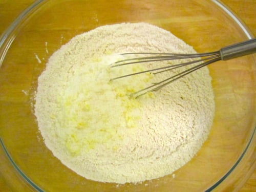 Mixing bowl with flour and melted butter being combined using a whisk.