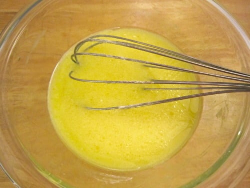 Whisk mixing beaten eggs in a glass bowl on a wooden surface