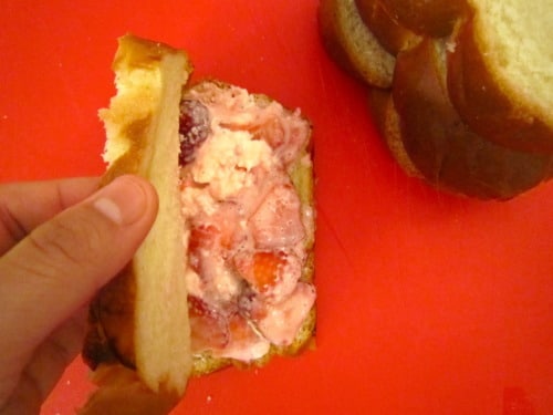 Slice of bread being filled with a creamy strawberry mixture for stuffed French toast.