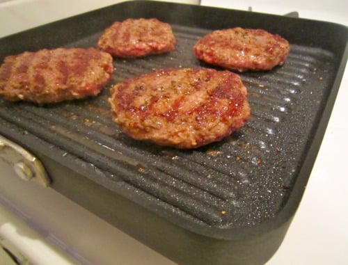 Juicy beef burger patties cooking on a stovetop grill pan.
