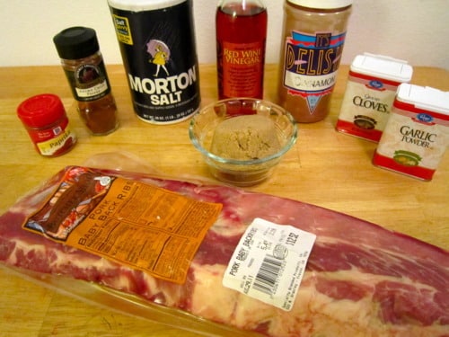 Raw baby back ribs with various seasonings and ingredients, including salt, brown sugar, spices, and red wine vinegar, arranged on a wooden surface.