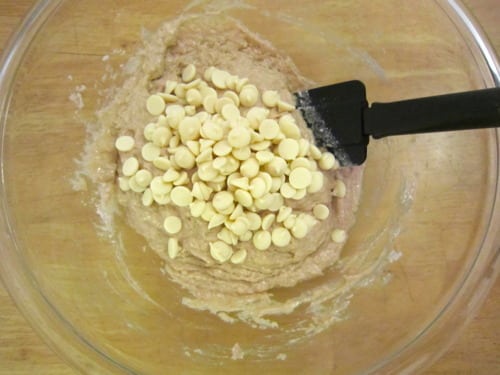 Pancake muffin batter in a glass bowl with white chocolate chips being folded in using a spatula.