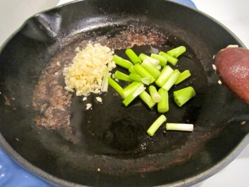 Chopped garlic and green onions in a black skillet, beginning to sauté.