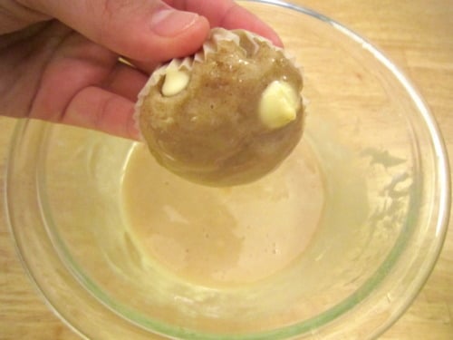 White chocolate chip pancake muffin being dipped into maple syrup glaze.