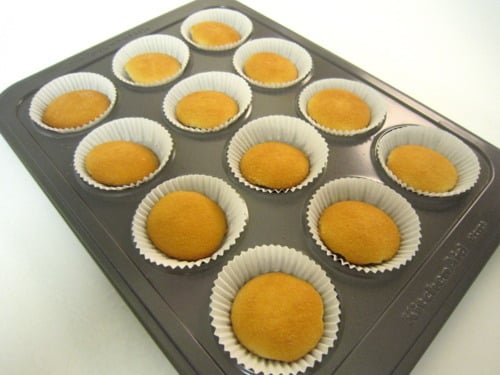 Mini vanilla wafer crusts in paper liners inside a muffin tin, prepared for strawberry cheesecake muffins.