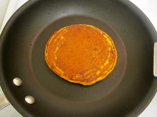 Pumpkin spice pancake cooking in a nonstick skillet, golden brown and evenly cooked.