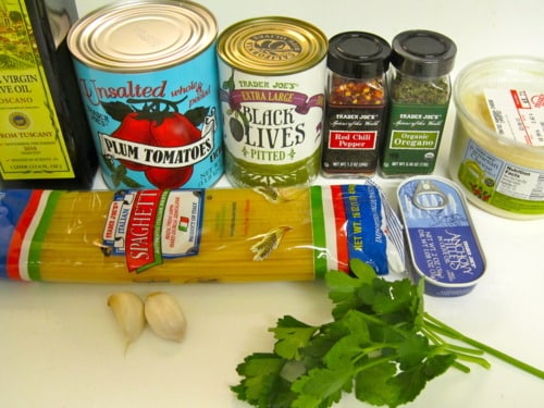 Ingredients for spaghetti alla puttanesca including spaghetti, canned plum tomatoes, black olives, capers, garlic, olive oil, chili flakes, oregano, anchovies, and fresh parsley.