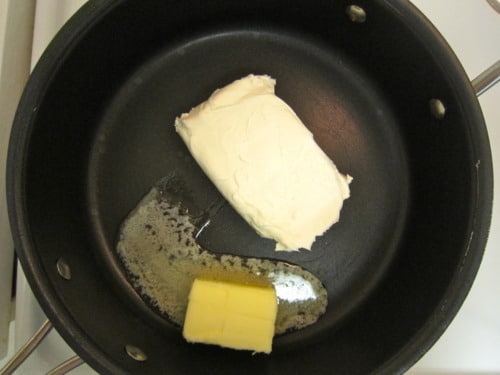 Meatball sub sandwich topped with melted cheese and marinara sauce, served with a side of potato chips on a white plate.