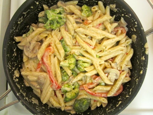 Creamy Alfredo pasta with penne, broccoli, mushrooms, and red bell peppers in a skillet.