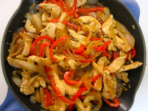 Skillet filled with cooked chicken strips, sliced red bell peppers, and onions seasoned and sautéed together.