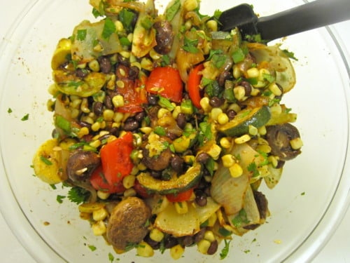 Mixed roasted vegetables with black beans, corn, peppers, onions, and herbs in a glass bowl.