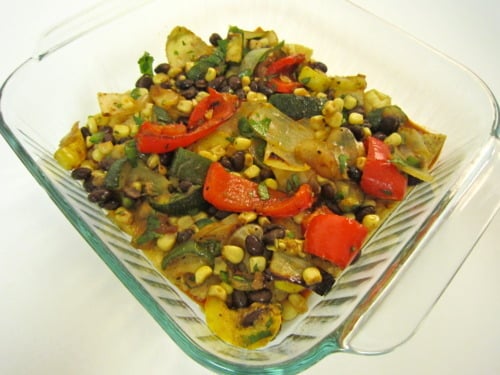 Glass baking dish filled with roasted vegetables, black beans, corn, and peppers for stacked roasted vegetable enchilada.