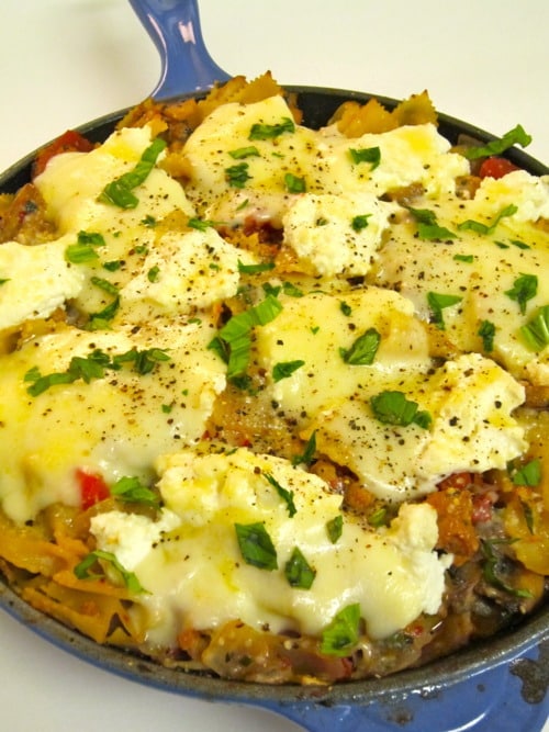 Skillet lasagna topped with melted cheese, ricotta dollops, and fresh herbs.