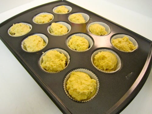 Muffin batter portioned into paper liners in a nonstick muffin pan, ready for baking jam-filled muffins.