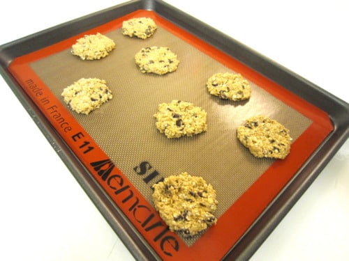 Unbaked banana oatmeal chocolate chip cookies on a silicone baking mat-lined baking sheet.