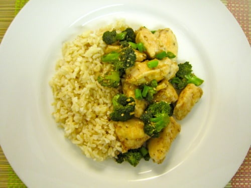 Lighter sesame chicken with broccoli served alongside brown rice on a white plate.