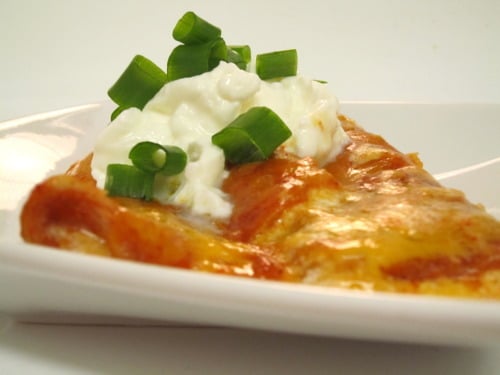 Slice of sour cream enchilada topped with sour cream and chopped green onions.