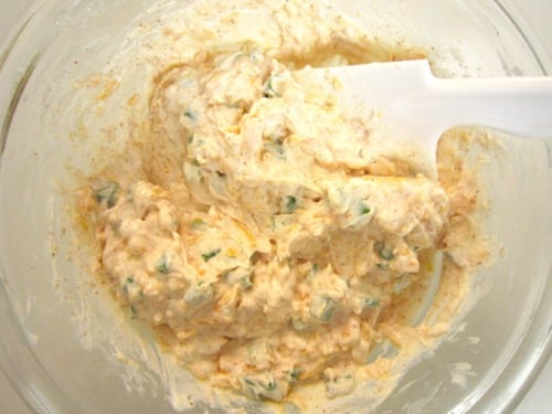 Creamy sour cream enchilada filling mixed in a glass bowl with visible herbs and seasoning, being folded with a spatula.
