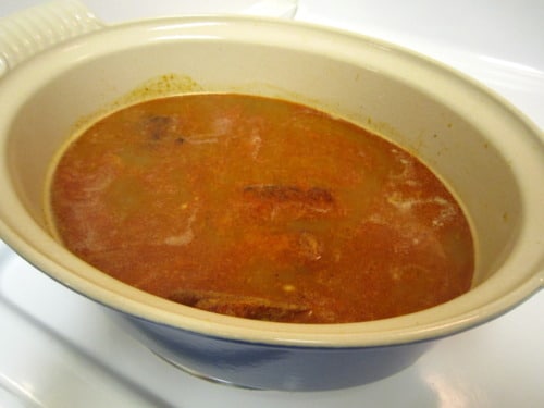 Pork carnitas simmering in a slow cooker with orange and beer-infused broth.