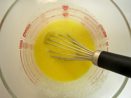 Glass measuring cup with wet ingredients being whisked for jalapeño cornbread.
