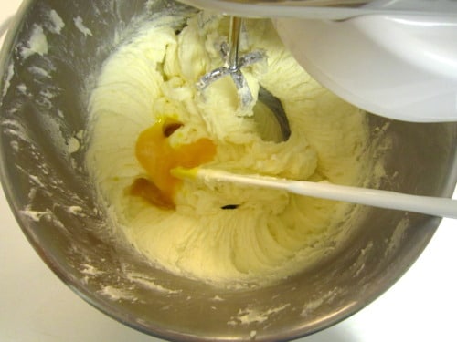 Butter cookie dough being mixed in a bowl with an electric mixer and added egg and citrus.