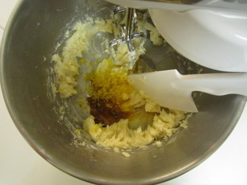 Cookie dough being mixed in a stand mixer bowl with lemon zest and flavoring added for mini strawberry-filled lemon sandwich cookies.