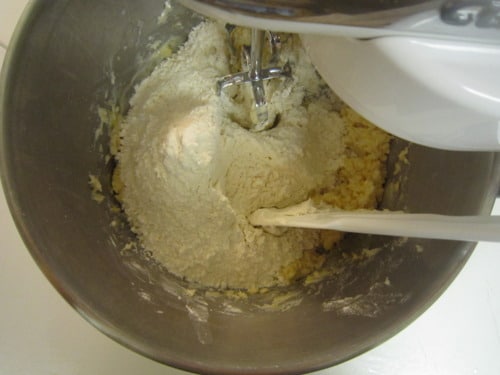 Flour being mixed into cookie dough in a stand mixer bowl with a beater attachment.