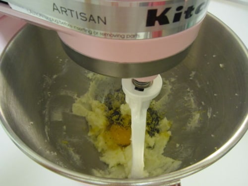 Stand mixer with paddle attachment mixing butter, sugar, egg, and poppy seeds for mini lemon poppy seed donut batter.