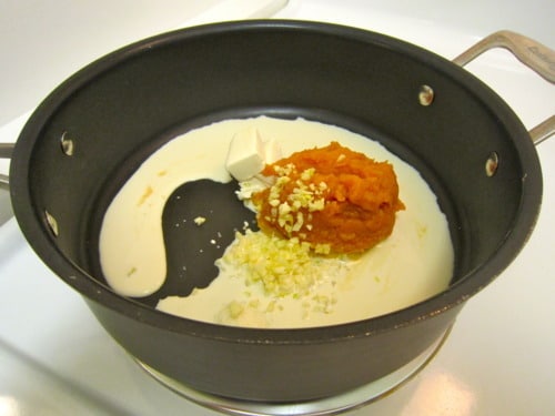 Heavy cream, pumpkin puree, butter, and minced garlic in a saucepan, prepared as the base for bacon and pumpkin pasta sauce.
