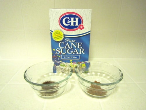 Box of powdered cane sugar behind two glass bowls containing ground coffee and cocoa powder for mocha muffins.