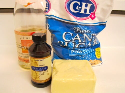 Ingredients for sweet champagne frosting, including peach champagne, powdered sugar, vanilla extract, and butter, arranged on a counter.