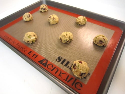 Cookie dough balls spaced on a silicone baking mat on a sheet pan, ready to be baked.