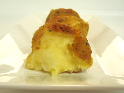 A close-up of a crispy fried mashed potato ball with a soft, cheesy center.