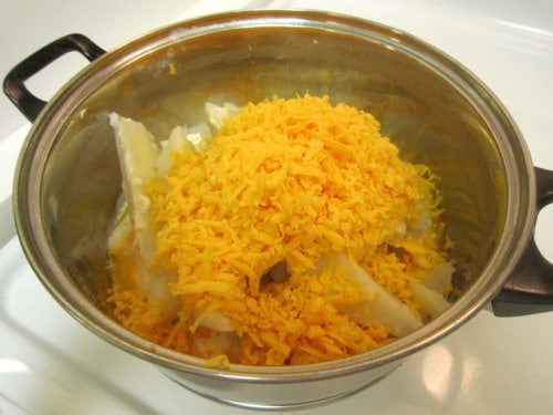 Shredded cheddar cheese and sliced potatoes in a pot for fried garlic cheddar mashed potato balls.