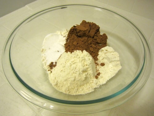 Flour, cocoa powder, sugar, and other dry ingredients combined in a glass bowl, prepared for chocolate buttermilk donut muffins with strawberry glaze.