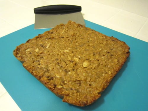 Homemade chocolate chip almond butter granola bars block on a cutting board with a bench scraper.