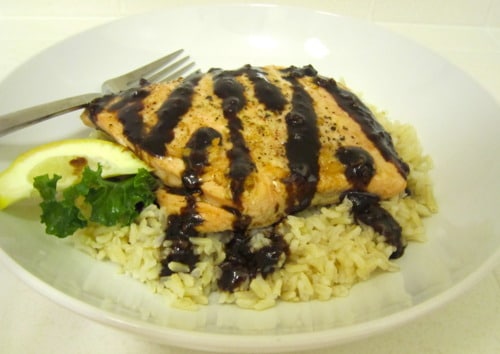 Salmon fillet with balsamic glaze served over brown rice, garnished with a lemon wedge and parsley.