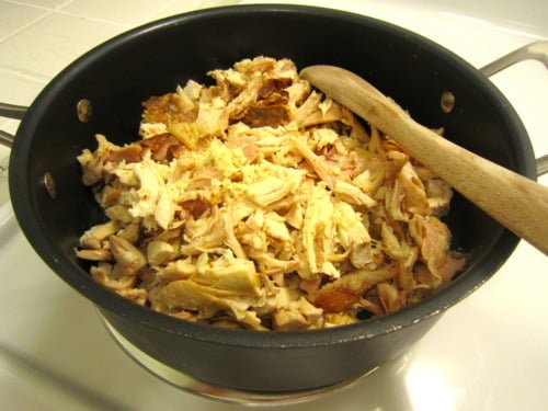 Shredded cooked chicken in a pot with a wooden spoon.