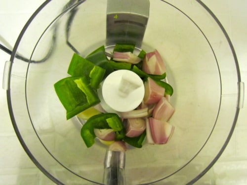 Chunks of green bell pepper and shallot placed in a food processor bowl.