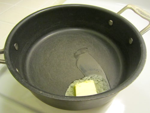 Butter melting in a black saucepan on a stovetop.