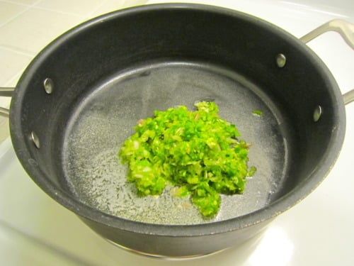 Chopped jalapeños sautéing in a black saucepan for chicken with jalapeño cream sauce.