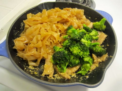 Skillet with cooked rice noodles, broccoli, and marinated pork for homemade pad see ew.