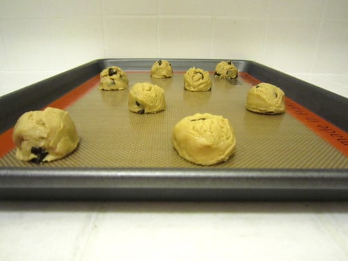 Portioned chocolate chip cookie dough balls spaced on a lined baking sheet, ready to be baked.