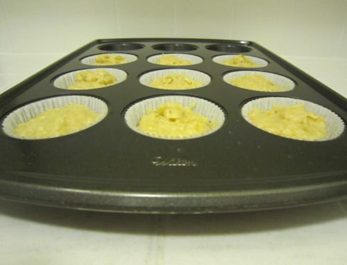 Banana orange coconut muffin batter portioned into paper liners in a nonstick muffin pan, viewed from a low angle before baking.